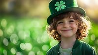 Happy young child with curly hair wearing green shamrock hat smiling outdoors with bokeh background for St. Patrick's Day celebration and Irish holiday festivities.