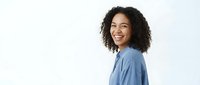 Young woman with curly dark hair and medium skin tone wearing light blue shirt, smiling at camera against white background for portrait and professional use.