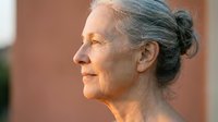 Senior woman with gray hair in bun, profile view, mature skin texture, peaceful expression, warm natural lighting, suitable for healthcare, wellness, aging, and lifestyle editorial use.