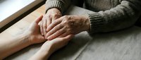Elderly hands gently holding younger hands in caring gesture showing intergenerational support, comfort and family connection on wooden table.