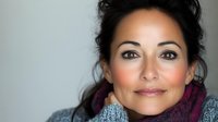 Close up portrait of smiling Hispanic woman with dark hair wearing gray sweater and purple scarf against light background. Natural makeup and warm expression convey confidence.