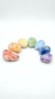 Polished tumbled stones in rainbow colors arranged in a circle on white background, isolated for wellness, healing, and spiritual design projects.