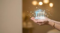 Female hands holding glowing digital bank building with sparkles representing financial services, banking technology and investment concepts.