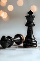 Black chess king piece standing victorious over fallen pawn with soft bokeh lights in background, symbolizing strategy, leadership and victory in business.