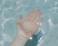 Wet hand palm up resting on clear turquoise pool water surface with gentle ripples and light reflections, summer freshness concept.