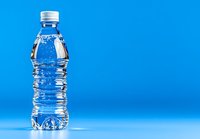 Clear plastic water bottle with rippled texture against vibrant blue background, showcasing pure mineral water with reflective surface and white cap.