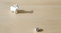 Miniature white goat and small gray mouse figurines casting shadows on light wooden surface, isolated objects for design projects and creative compositions.