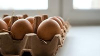 Fresh brown eggs in cardboard carton on kitchen counter near window with natural lighting for cooking and baking recipes.