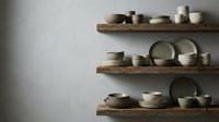 Minimalist kitchen interior with wooden floating shelves displaying ceramic dinnerware and pottery against neutral wall for modern home decor.