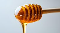 Golden honey dripping from wooden dipper stick against white background. Natural sweetener flowing in amber streams for culinary and health applications.