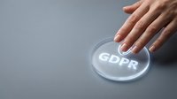 Hand pressing a glowing GDPR button on gray background, symbolizing data protection compliance and privacy regulation concept.