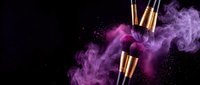 Luxury makeup brushes with golden handles surrounded by vibrant purple and pink powder explosion on black background for cosmetic advertising.