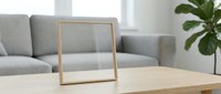 Empty wooden picture frame on coffee table in modern living room with gray sofa and green plant for home decor and interior design mockup.