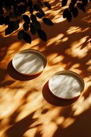 Sunlight and leaf shadows cast dramatic patterns over minimal ceramic bowls with cream interior on warm brown background, creating artistic play of light and dark.