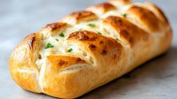 Freshly baked braided bread loaf with golden brown crust and herbs on marble surface for bakery menu design and culinary marketing materials.