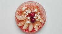 Fresh pink grapefruit slices arranged on plate with bright red cherries and white cheese crumbles, top view of healthy breakfast composition on light background.