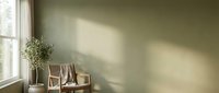 Minimalist living room interior with natural sunlight streaming through window creating soft shadows on sage green wall with wooden chair and plant.