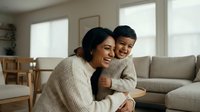 Young South Asian mother and son sharing a warm hug in a cozy living room, both smiling joyfully, capturing family love and togetherness.