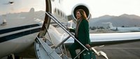 Young professional woman in green blazer boarding private jet at sunset airport with mountains in background for luxury business travel.