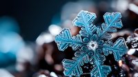 Macro close-up of intricate blue snowflake crystal with detailed hexagonal structure and delicate ice formations on dark blurred background for winter themes.