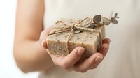 Caucasian woman holding handmade natural soap bar wrapped in kraft paper with twine bow and eucalyptus sprig, organic skincare concept.
