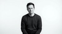 Professional Caucasian man in dark sweater sitting confidently against white background, business portrait for corporate branding and marketing materials.