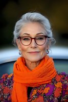 Elegant senior woman with silver hair wearing bright orange scarf and floral print blouse smiles confidently at camera, showcasing natural aging and vibrant style.