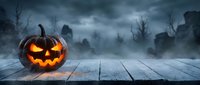 Glowing jack-o-lantern pumpkin on wooden table with spooky graveyard cemetery background. Halloween horror atmosphere with fog and tombstones.