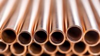 Copper pipes arranged in parallel rows showing circular ends and metallic texture. Industrial plumbing materials with warm bronze tones and reflective surfaces.