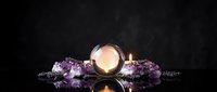 Spa wellness setup with burning candle, purple flowers and lavender sprigs on dark reflective surface for relaxation and aromatherapy treatments.