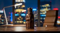 Wooden carved figurine of bearded man displayed on desk with laptop and blurred city skyline lights in background, suitable for office decor and business themes.