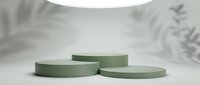 Minimalist sage green cylindrical podiums on white surface with soft lighting and botanical shadows for product display and branding presentations.