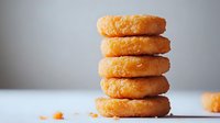 Stack of glazed donuts on white surface against neutral background, with soft natural lighting highlighting golden texture and sugar coating. Macro food photography.