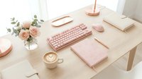 Feminine pink workspace setup with keyboard, mouse, notebook and coffee cup on wooden desk. Stylish home office arrangement for productivity and creativity.