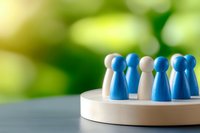 Blue and white wooden game pieces arranged in circle on round platform against blurred green background representing teamwork, leadership and inclusion.