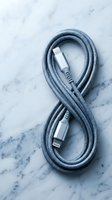 Gray braided charging cable with metal connectors arranged in figure eight pattern on white marble surface for tech accessories and electronics.