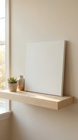 Blank white canvas on wooden floating shelf with small succulent plant and ceramic vase in minimalist interior with natural window light for mockup design.