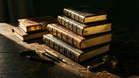 Stack of antique leather-bound books with ornate golden spines and vintage fountain pen on wooden surface creating scholarly atmosphere for education content.