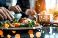 Professional chef plating gourmet dish with herbs and vegetables in modern kitchen with warm bokeh lighting for culinary presentation and fine dining.