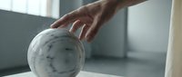 Hand reaching for white bowling ball with finger holes on wooden lane surface in modern bowling alley interior with soft natural lighting.