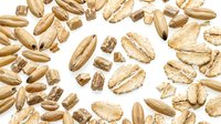 Whole and crushed oat grains scattered on white background, showcasing natural texture and organic cereal seed detail for food and nutrition concepts.