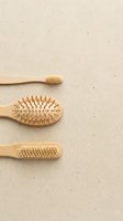 Natural bamboo eco-friendly personal care tools including toothbrush, hair brush and massage brush on neutral beige textured background for wellness.