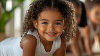 Young African American girl with curly hair and bright smile wearing white tank top, looking at camera with natural joy and confidence in home setting.