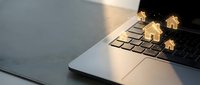Wooden house models on laptop keyboard representing real estate technology, property search, online mortgage applications, and digital home buying services.