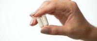 Hand holding white medical capsule pill between fingers on clean background for healthcare and pharmaceutical concepts.