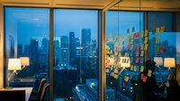 Modern office workspace with floor-to-ceiling windows overlooking illuminated city skyline at dusk, featuring colorful sticky notes on glass for brainstorming and project planning.