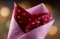 Red napkin with golden heart pattern folded in pink wrapper against soft bokeh background, romantic table setting for Valentine's day celebration or wedding decor.