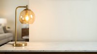 Brass table lamp with amber glass globe shade on marble surface, warm lighting for modern home decor and interior design.