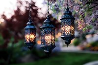 Glowing vintage lanterns with ornate metalwork hanging outdoors at dusk, creating magical ambiance under flowering tree branches with soft bokeh background.