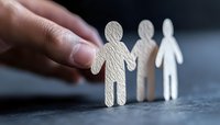 Hand holding small white paper cutout figures in chain formation against dark background, symbolizing unity, teamwork and human connection.